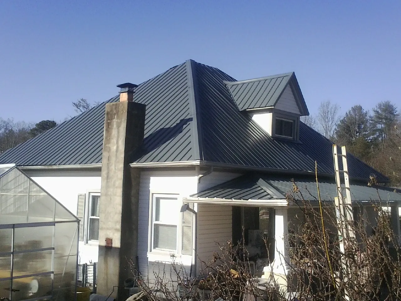 Dark blue standing seam metal roof on a white farmhouse with dormer — Slate & Tile Roof Repair by Roofing Brothers in Spindale