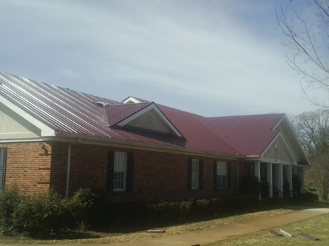 Red metal roof with gabled entries on a long brick building, from a Hail Damage Roof Repair job in Spindale