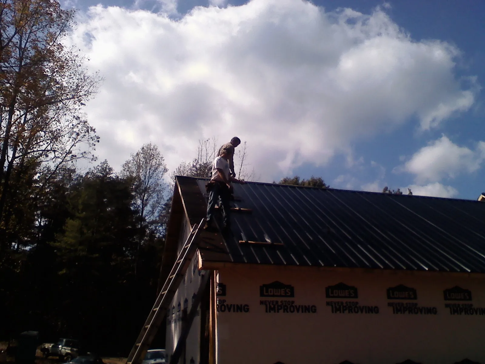 Roofer fastening dark metal panels high against a cloudy sky, from a Roof Inspection job in Spindale